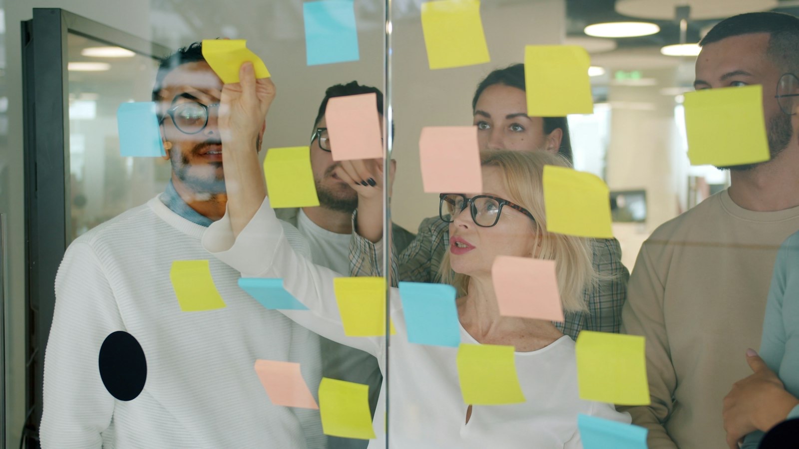 A small team planning with sticky notes on a glass wall.